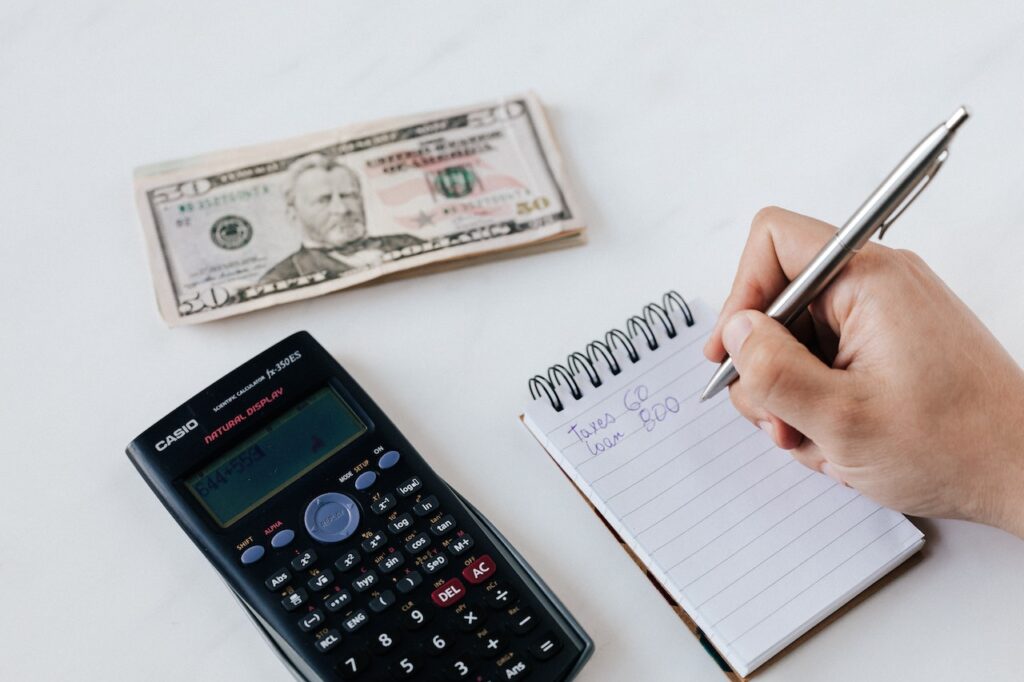 calculatrice, argent et bloc note avec une liste des charges financières pour montrer l'offre livret et compte épargne de Distingo
