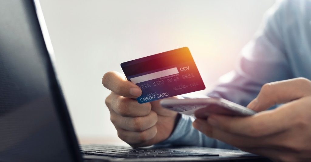 un homme tenant sa carte bleue avec son ordinateur